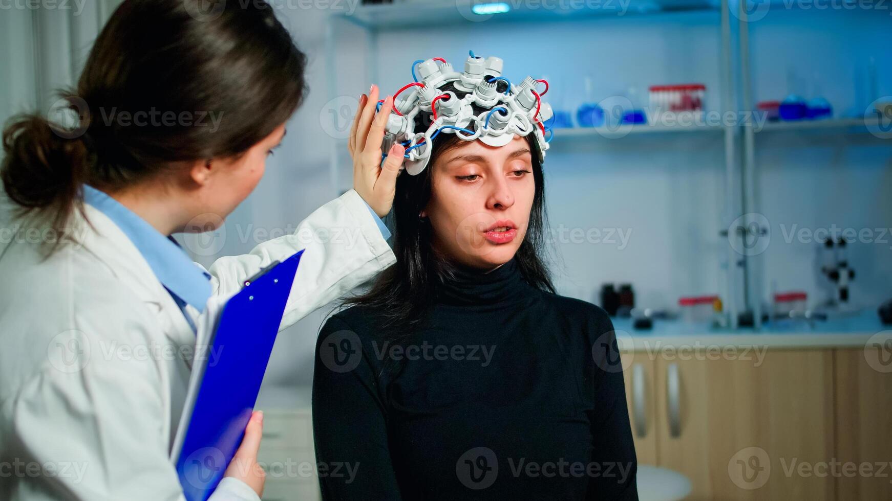 Patient with eeg headset discussing with medical researcher during examination sitting on chair in neurological laboratory. Doctor monitoring nervous system, descovering diagnosis of disease. photo