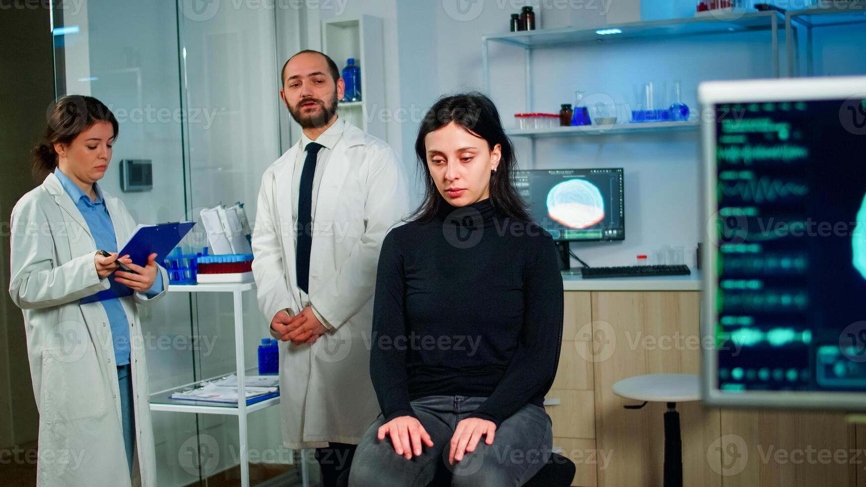 Team of scientists specializing in neurological medicine discussing health status of patient, brain functions, nervous system, tomography scan while woman waiting diagnosis of disease sitting in lab photo