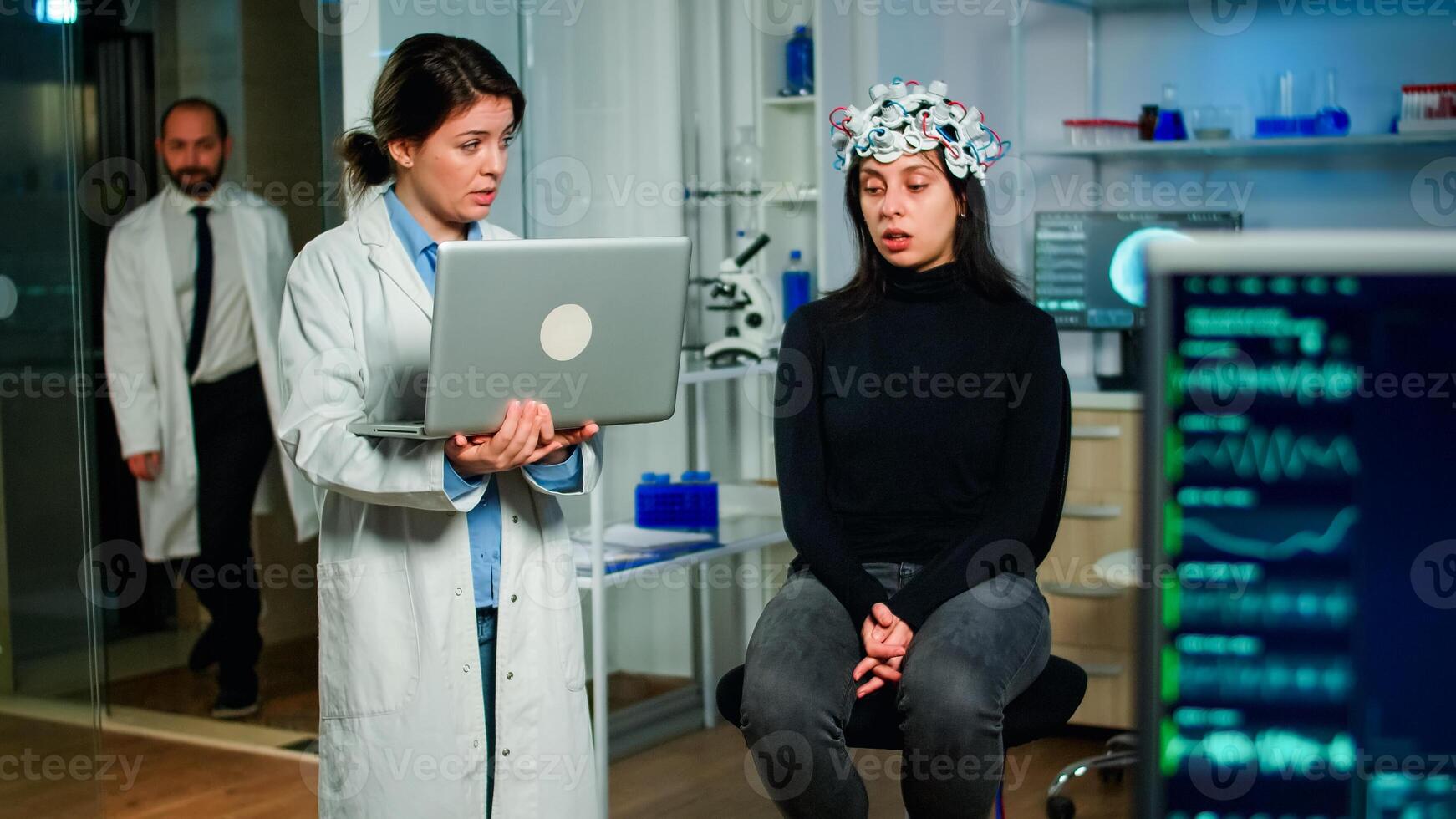 Medical neurologist doctor asking symptoms of patient taking notes on laptop, woman wearing high tech brain scanner. Researcher scientist controlling EEG headset analyzing nervous system functions photo