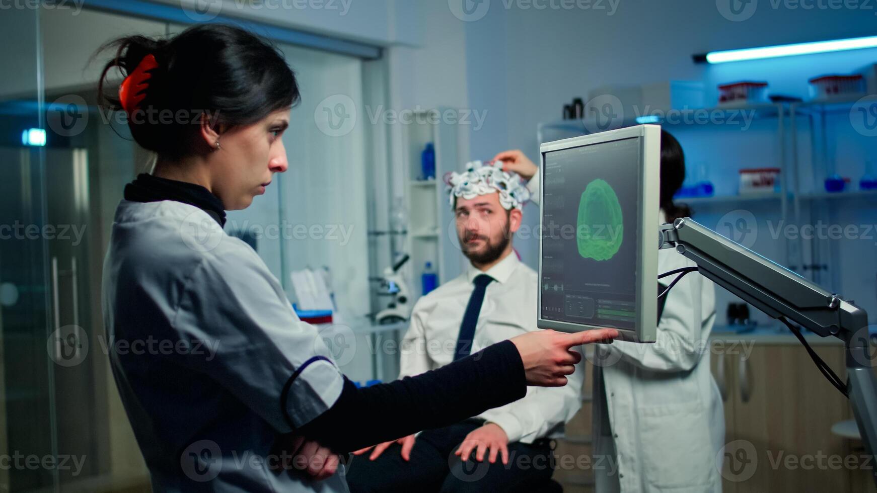 Woman researcher looking at monitor analysing brain scan while coworker discussing with patient in background about side effects, mind functions, nervous system, tomography scan working in laboratory photo