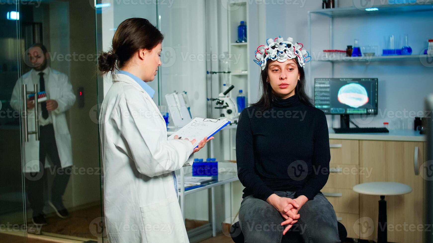 Neurologist doctor asking symptoms of patient taking notes on clipboard, adjusting high tech brain scanner. Medical scientist controlling EEG headset analyzing brain functions and health status photo