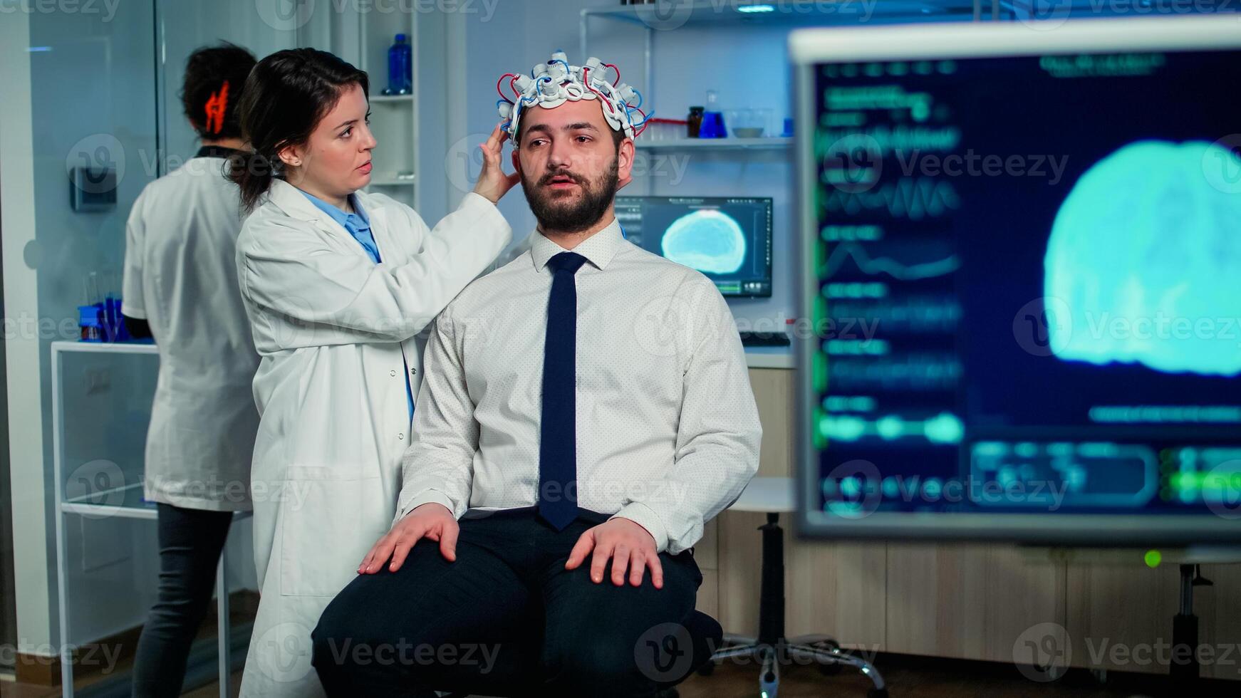 Medical researcher putting performant brainwave scanning headset monitoring brain functions in medical neurological laboratory with monitor showing eeg scan. Treating nervous system dysfunctions photo