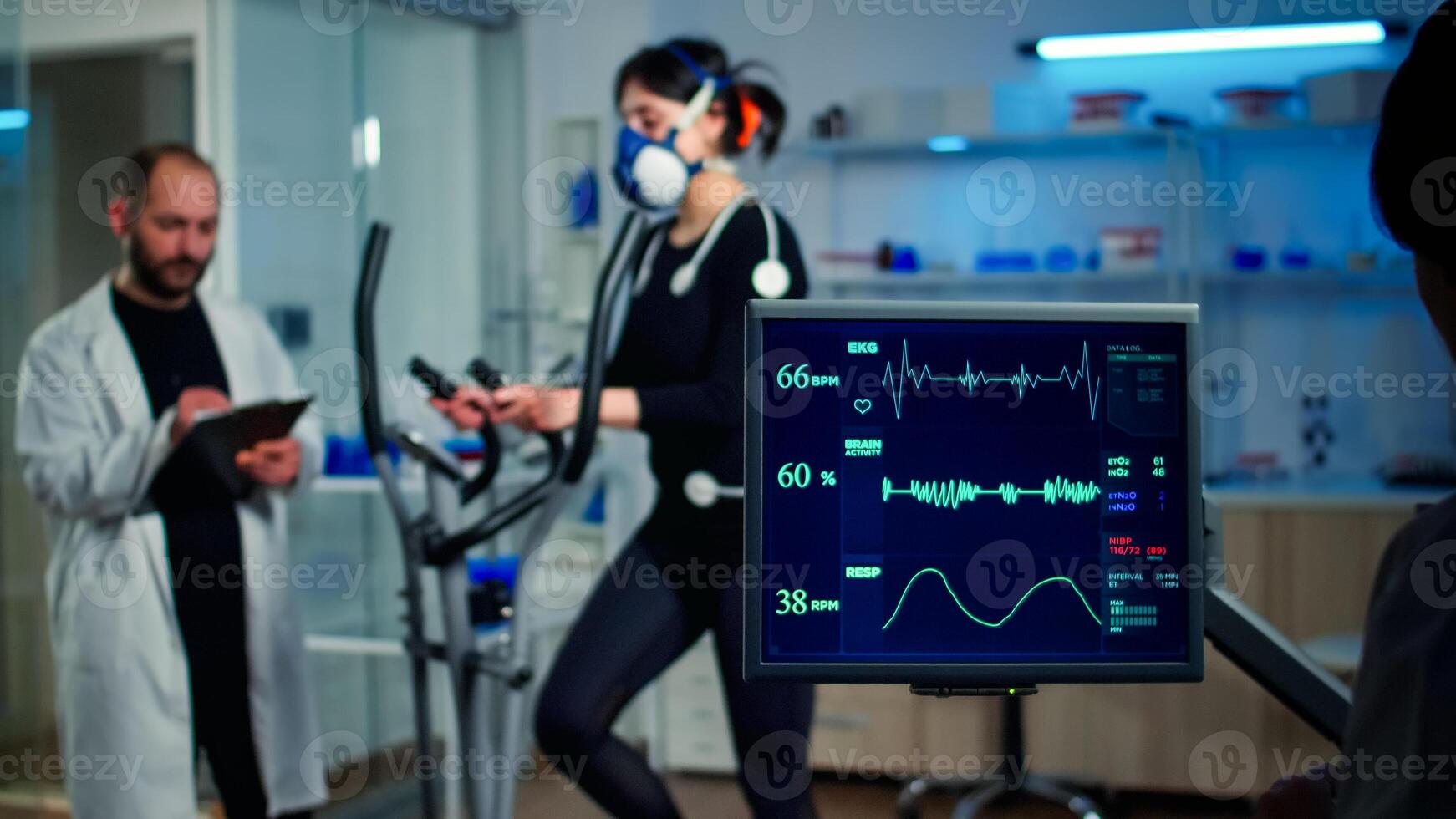 Specialist sport researcher monitoring heart rate on athlete while woman with mask running on cross trainer talking with medical doctor. Physician using tablet controling EKG data in modern laboratory photo