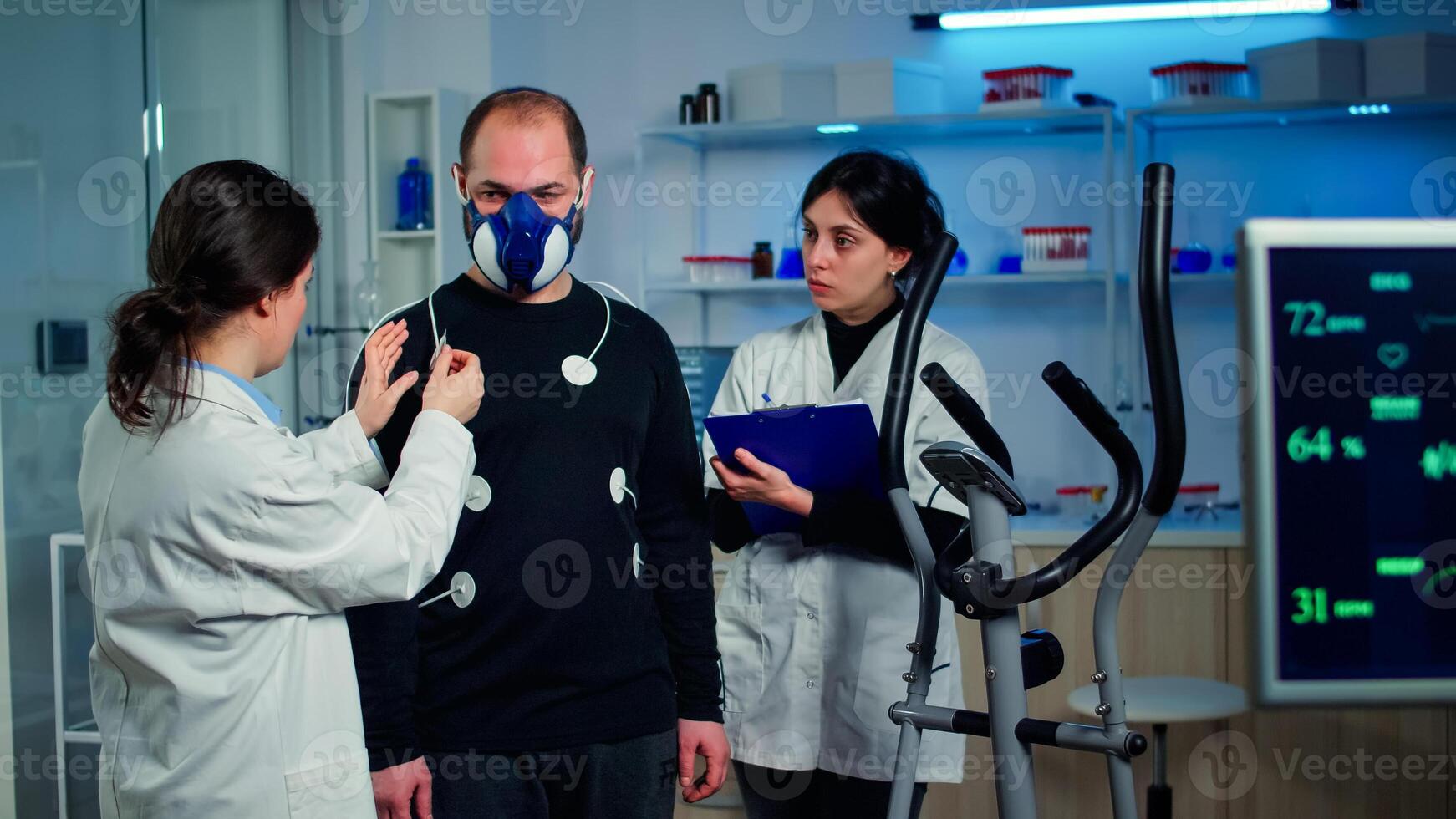 Scientist researcher preparing man patient for endurance test attaching electrodes on professional body equipment. Team of doctors monitoring health of sportsman with mask, heart rate and vo2 photo