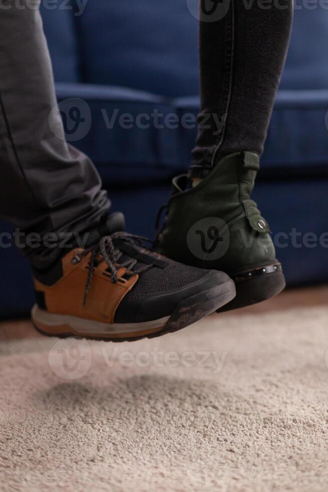Happy cheerful friends touching feet keeping social distancing greeting eachother wearing face mask preventing spread of coronavirus holding beer bottles in apartment living room. Conceptual image. photo