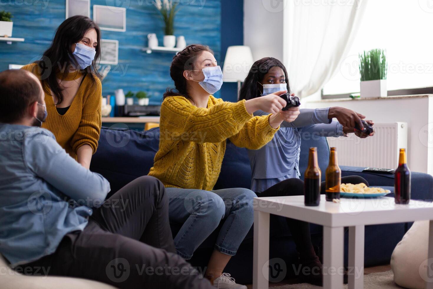 Mixed race friends meeting to playing games with wireless controller wearing face mask to prevent getting sick with corona in time of social pandemic. Group of people enjoying time together. photo