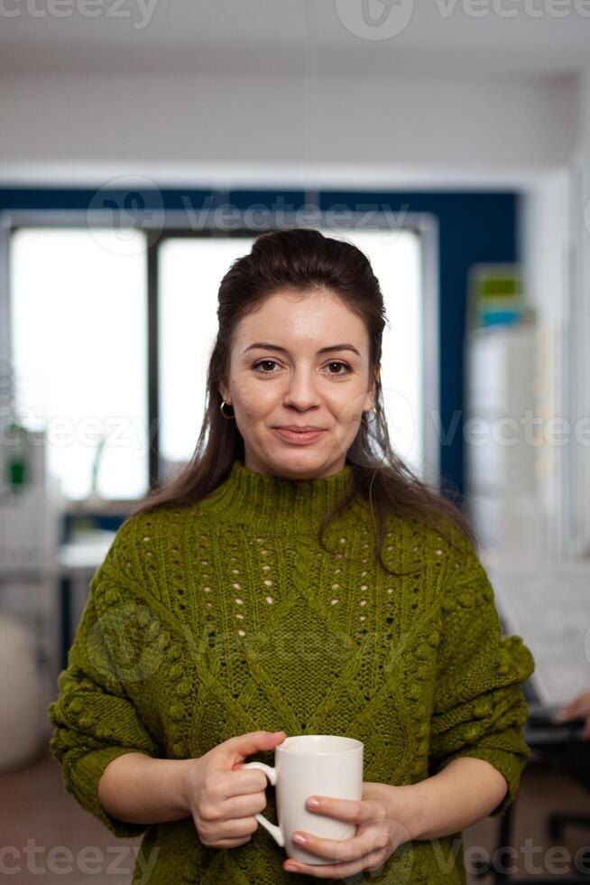 Portrait of designer artist smiling at camera holding cup of coffee standing in start up multimedia agency office. Woman working in creativity studio production editing design with diverse team. photo