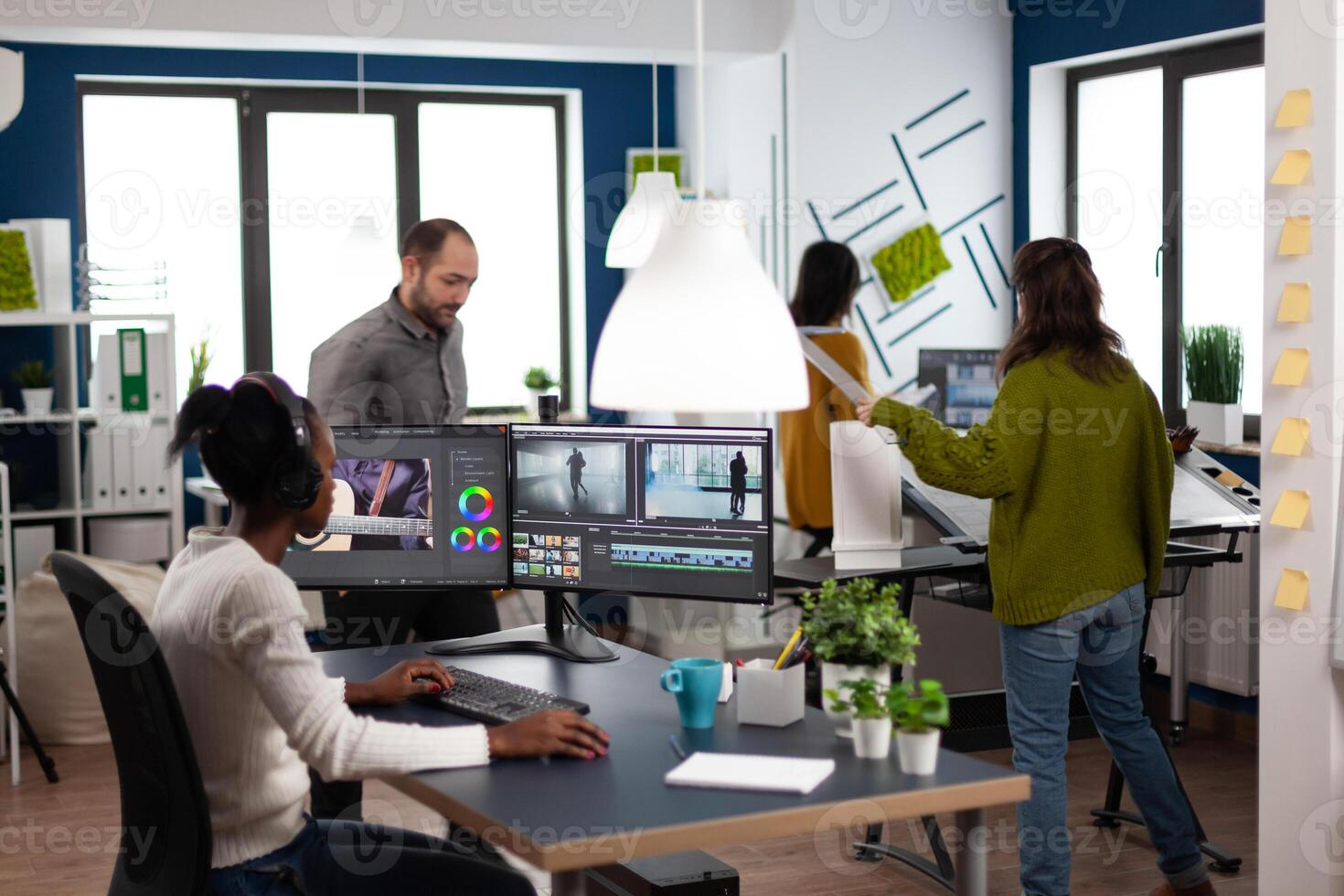 African american editor wearing headset editing movie using post production software working in start up company office. Black creator processing footage on computer with dual displays photo