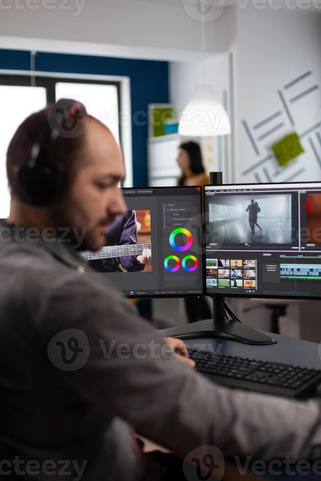 maker with headset working with footage and sound on pc with two displays, taking notes while editing customer creative . Man editor processing film montage in startup agency office. photo
