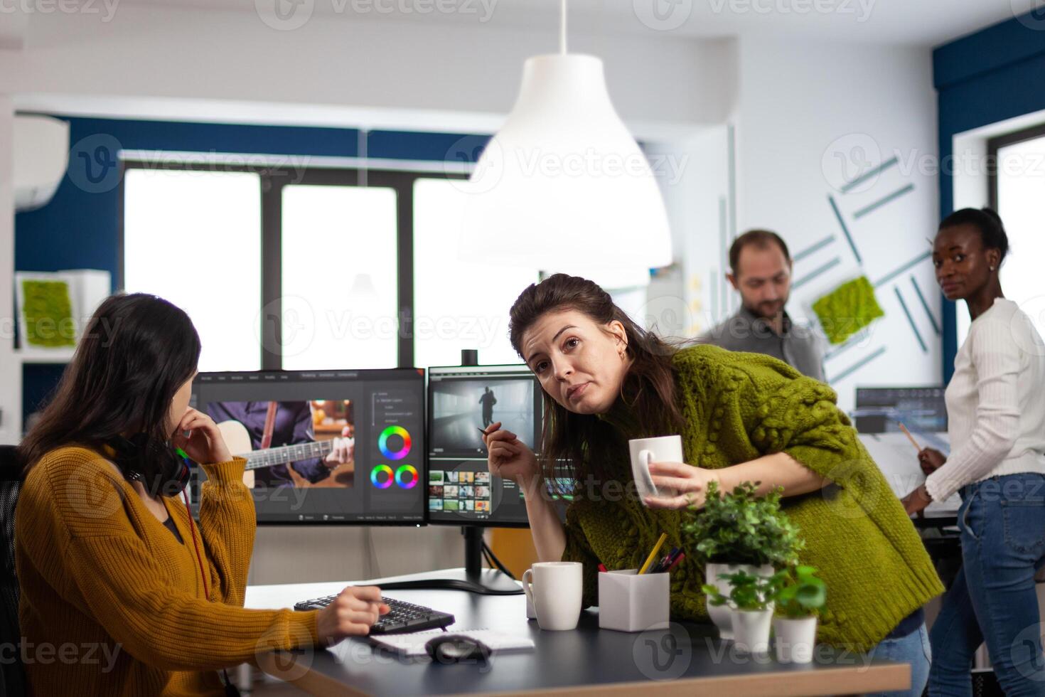 Team discussing about movie project looking at film footage working in creative start up agency office with two monitors. Videographers processing montage with post production software photo