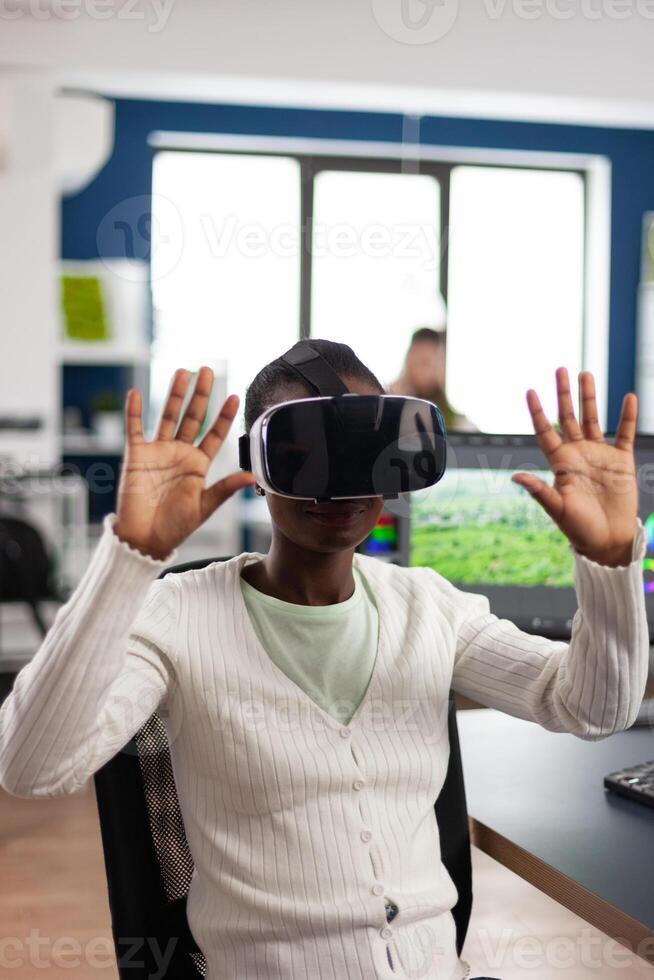 African maker experiencing VR headset, gesturing, editing film montage working at footage and sound on computer with two displays. Videographer processing movie in creative agency photo