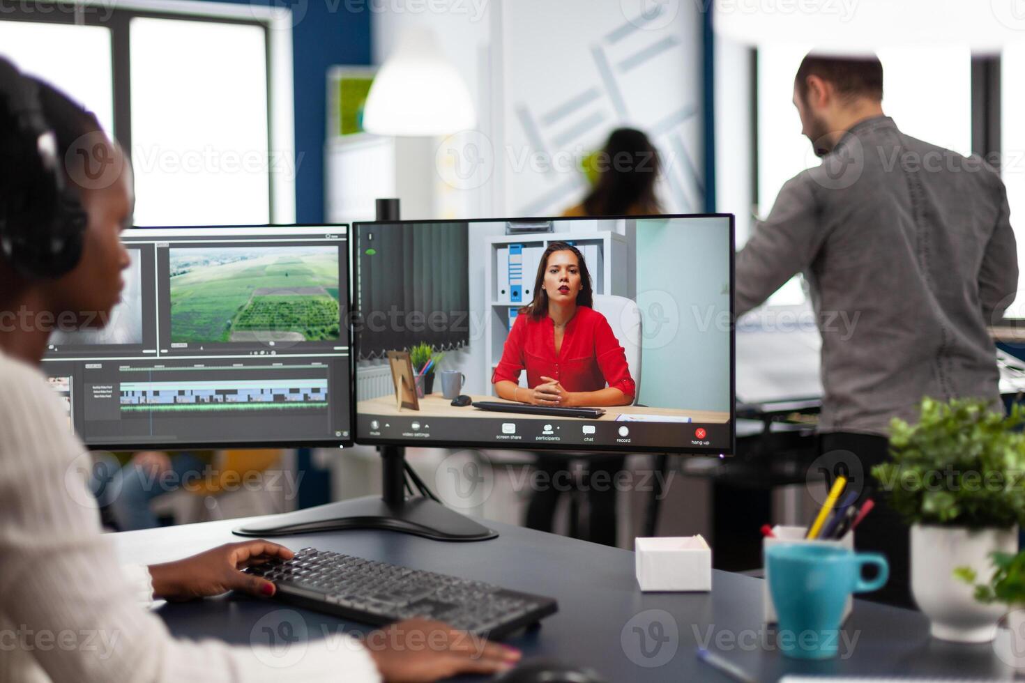 editor in web online conference with project creator on call editing business client work, getting feedback on movie using post production software on two monitors in start up office photo