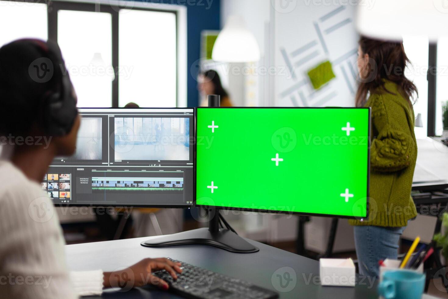 African woman multimedia content creator with headphones processing film montage working at greenscreen, chroma key isolated display of computer. Videographer editing movie in post production software photo