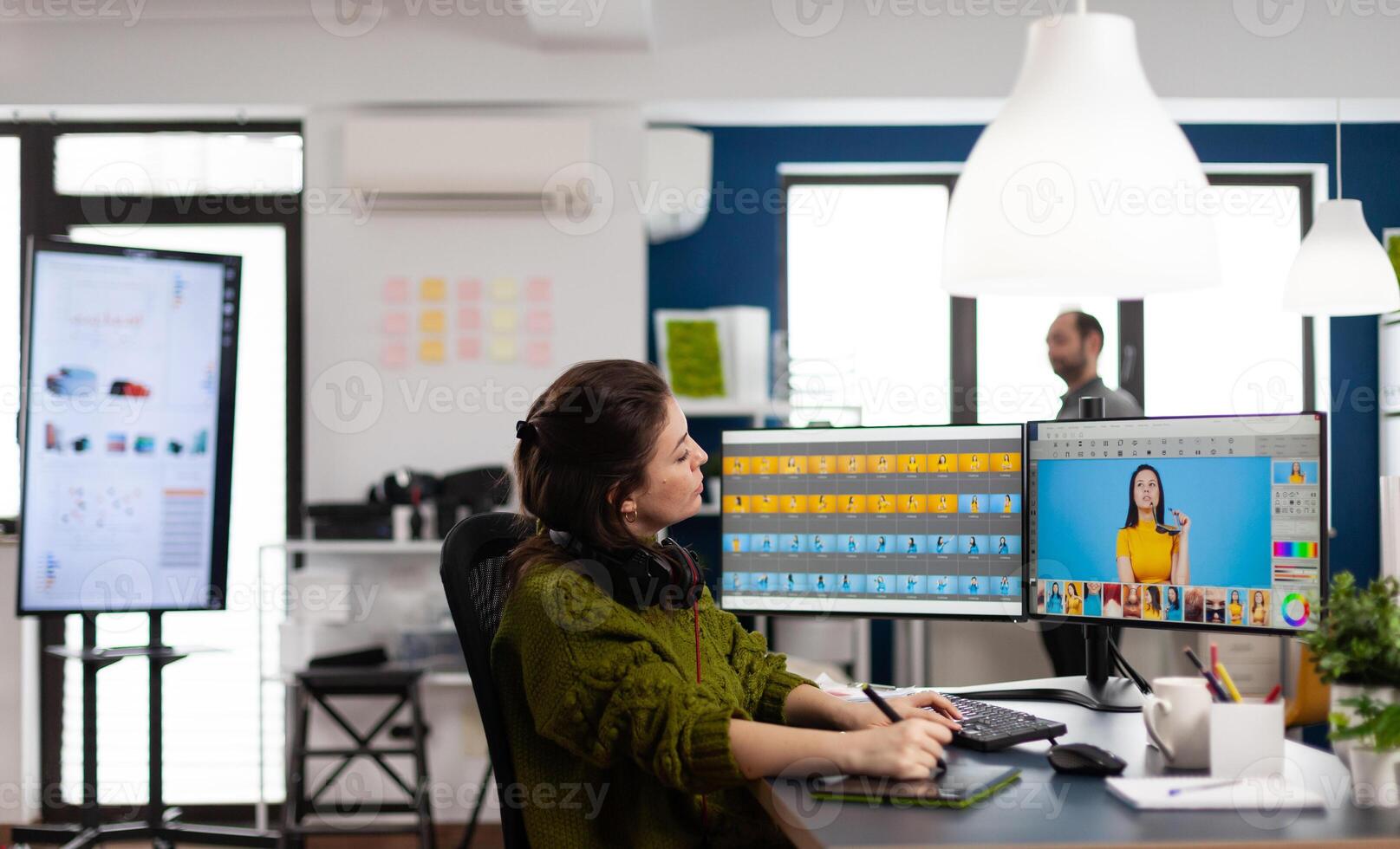 Creative photographer using digital retouching software, wearing headphones editing photos for client. Stylish retoucher, graphic editor working in creative multimedia workplace