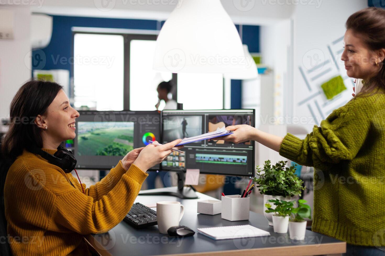 Creators drinking coffee and talking during office break sitting at desk in digital agency studio. editor and sound engineer working at movie project, editing film footage in software app photo