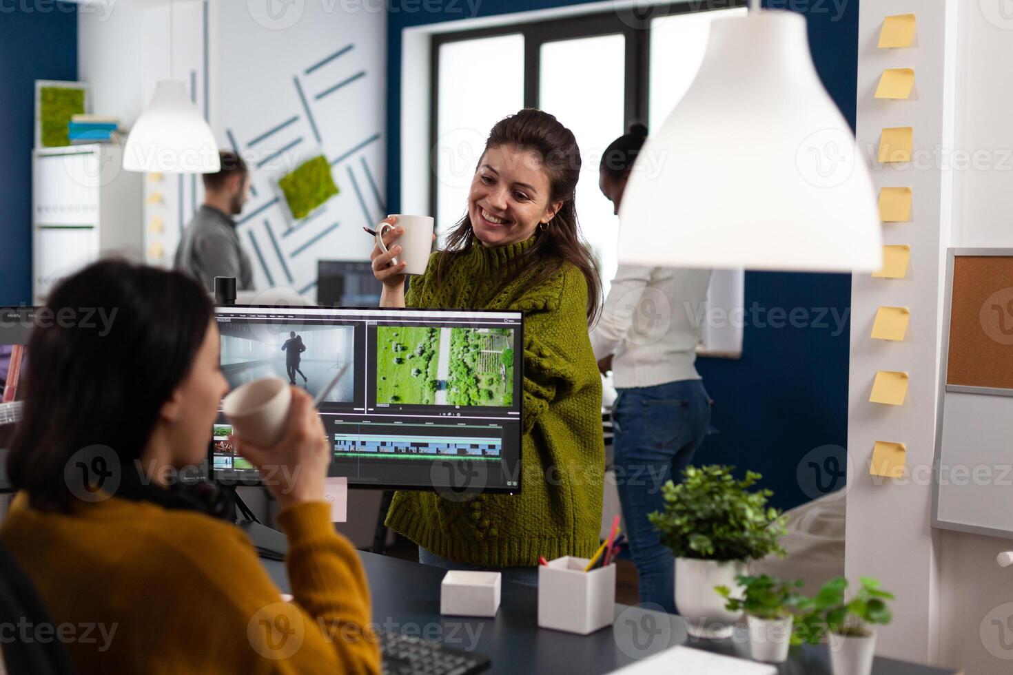 Team of multimedia content creators talking about project while drinking coffee working in editing app sitting at pc in digital production company. Videographer editor in startup agency photo