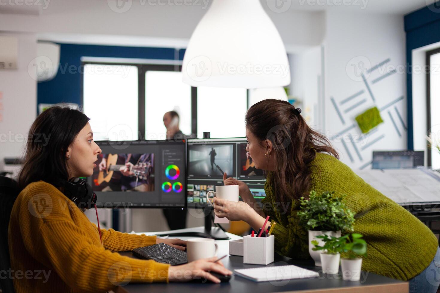 Happy coworkers talking about creative film montage looking at movie production ideas working in start up office with two monitors. Womens editors editing project in post production software photo