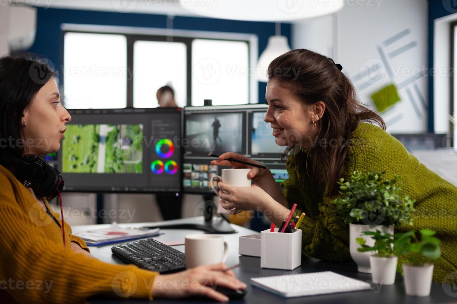 Videographer editing montage of film using modern software sharing ideas with coworker in startup studio office. Coworkers talking about creative process in post production agency photo