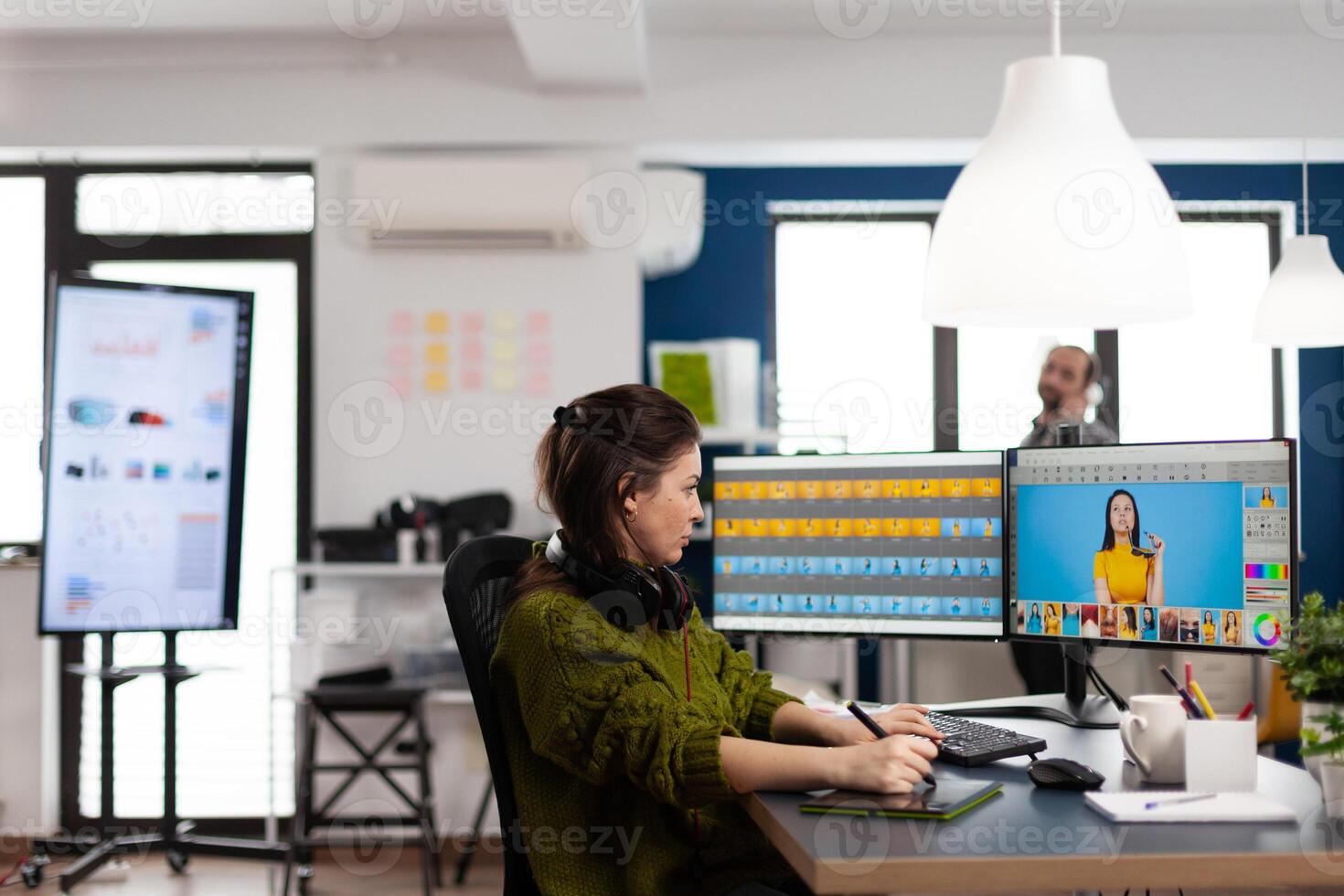 Creative photographer using digital retouching software, wearing headphones editing photos for client. Stylish retoucher, graphic editor working in creative multimedia workplace