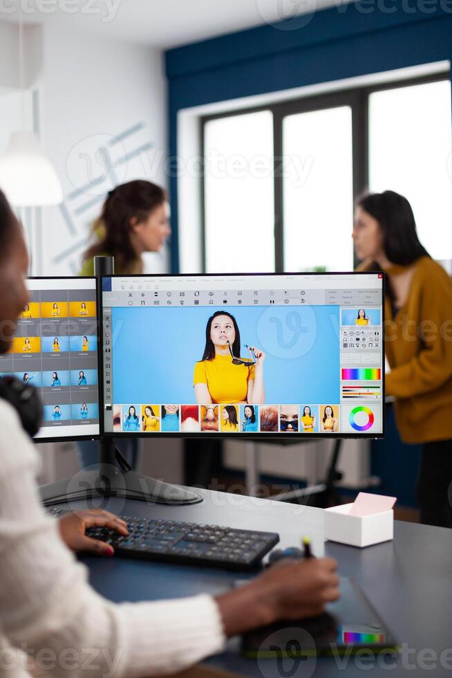 Black retoucher artist analysing images on pc with two monitors and retouching digital assets with stylus pencil. African designer using photo editing software working in creative production office