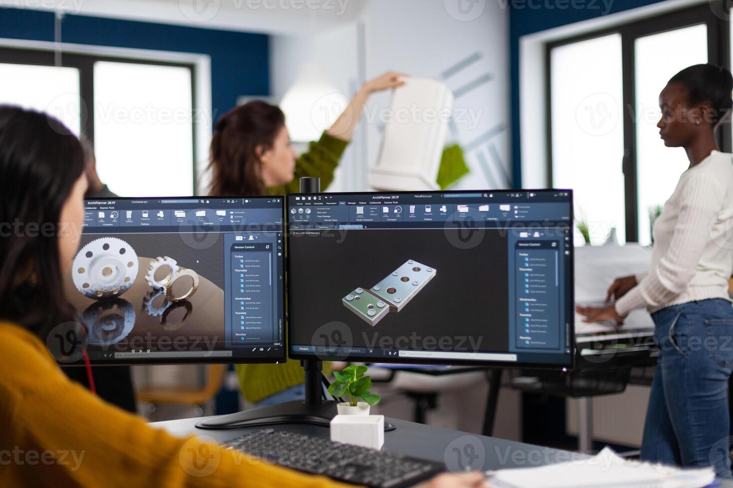 Industrial engineer woman working at pc with two monitors, screens showing CAD software with 3D architecture prototype of gears mechanical piece. Entrepreneur working in creative construction office photo