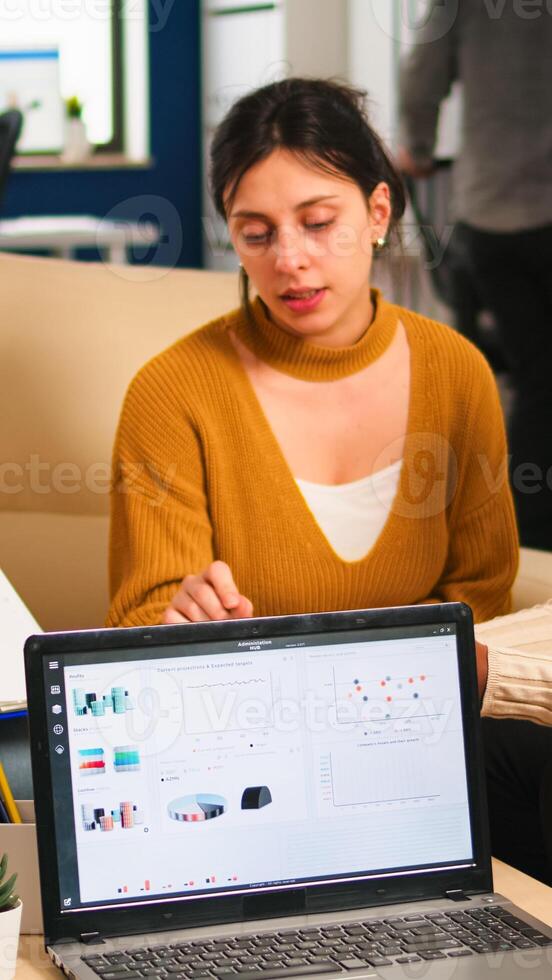 African woman talking about project, discussing start up ideas using pc, diverse employees gathered in co-working, working process in busy company. teamwork help concept photo
