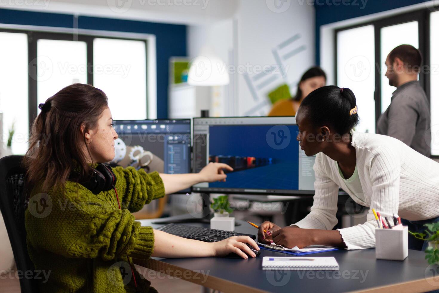 Diverse women game developers creating game interface sitting in startup creative production company pointing at pc displays. Workers developing online graphics games with modern technology photo