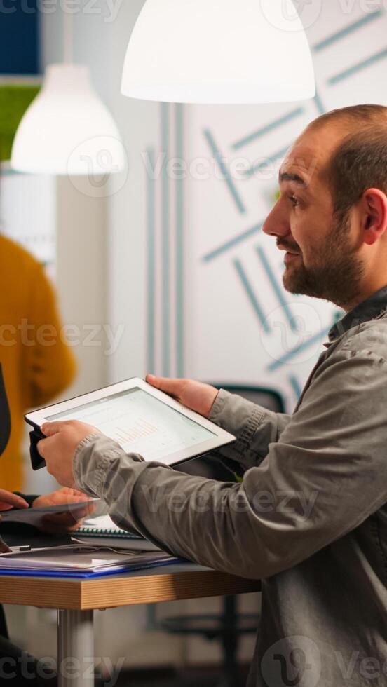 Startup diversity teamwork brainstorming sitting at desk in modern office, planning business strategy holding tablet searching management solutions. Team of multiethnic businesspeople working company photo