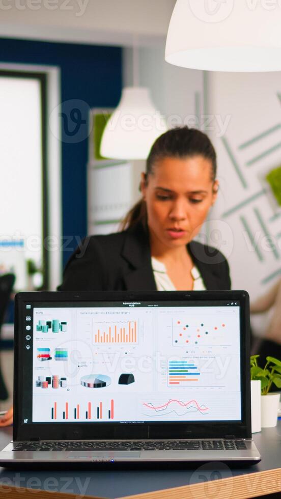 Team of colleagues employees cooperating sitting at desk in startup company office analysing graphs, taking notes. Business coworkers planning start up business project, brainstorming in wokrplace photo