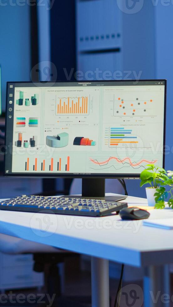 Empty start up business office with modern design during night with graphics running on the desktop. Financial company with nobody in it, place of work startup, workplace indoors concept photo