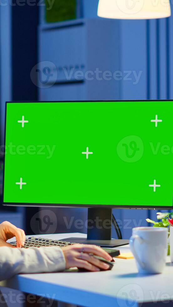 Woman looking at computer with chroma key during night time in start up business office working overtime. Freelancer watching desktop monitor mockup display with green screen, typing writting photo