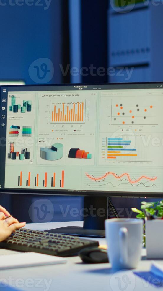 Busy woman working at night in front of computer taking notes writing on notebook annual reports, checking financial project. Focused employee using technology network wireless doing overtime for job photo