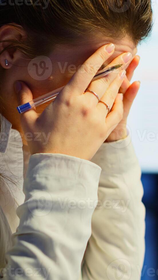 Close up of stressed busy woman with headache working from business office late at night. Tired focused employee using modern technology network wireless doing overtime for job checking reports photo