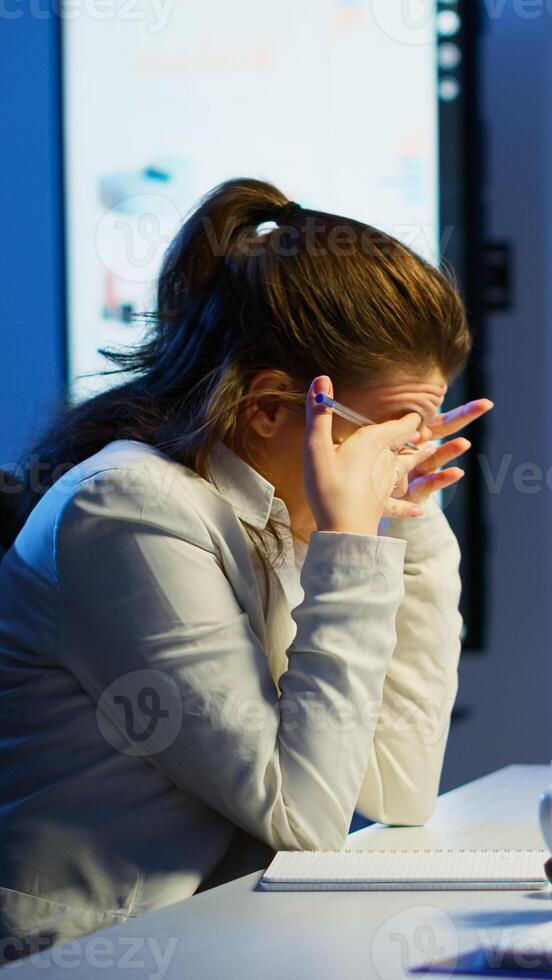Focused tired entrepreneur checking graphics from laptop writing on notebook working from business office overtime. Busy employee using modern technology network wireless reading typing, searching photo