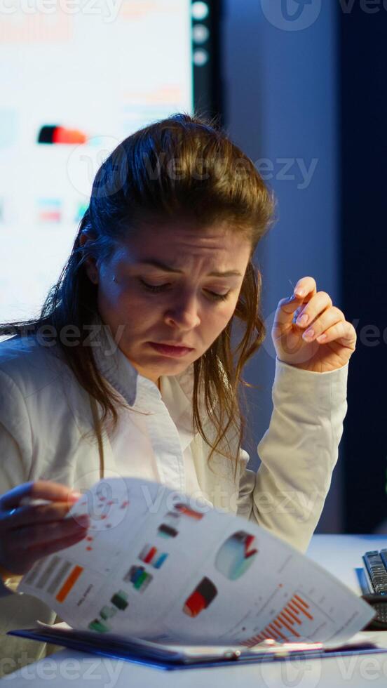 Tired freelancer comparing graphics from clipboard and computer working from business office overtime. Busy focused employee using modern technology network wireless reading typing, searching photo