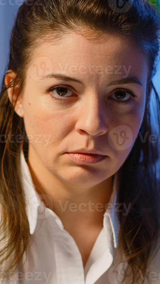 Close up of overworked business woman looking exhausted at camera sighing working late at night in start-up business office. Focused employee using technology network wireless doing overtime for job photo