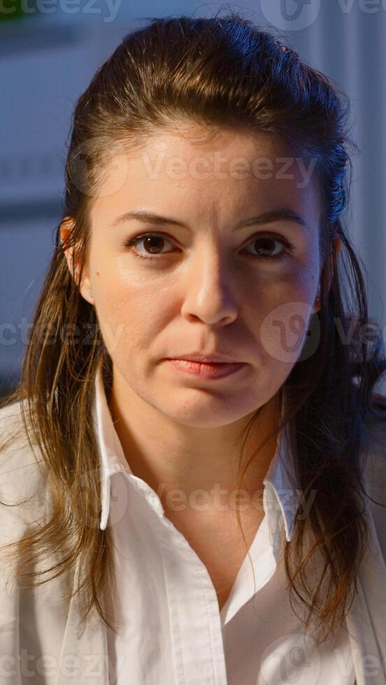 Portrait of employee having conference late at night overworking sitting in modern start-up office drinking coffee. Freelancer talking on virtual meeting at midnight doing overtime photo