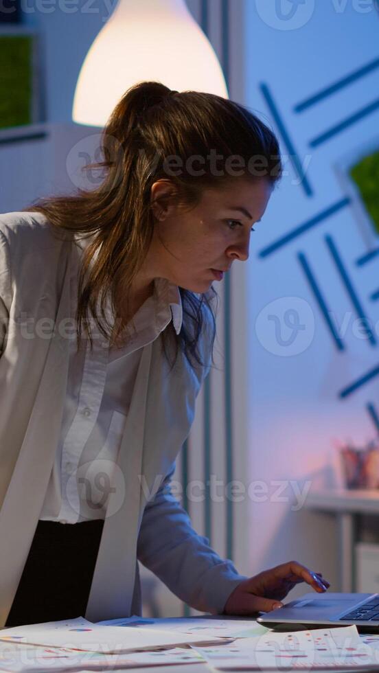Happy business woman working on financial reports pointing to numbers, looking at laptop checking statistics graphs, having good results, smiling standing at desk late at night doing overtime. photo
