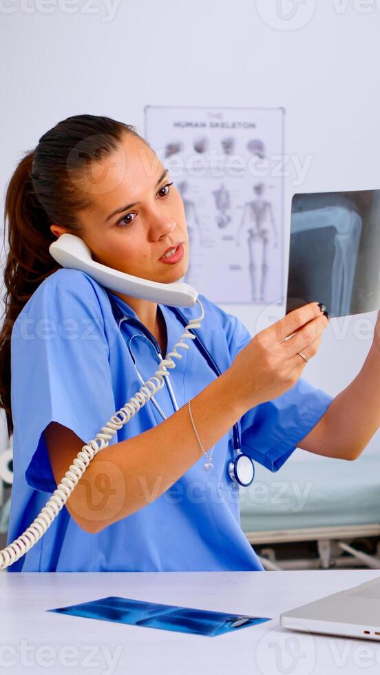 Nurse answering at hospital call checking the result of patient x-ray and diagnosing him. Healthcare physician in medicine uniform, receptionist doctor assistant helping with phone concultation photo