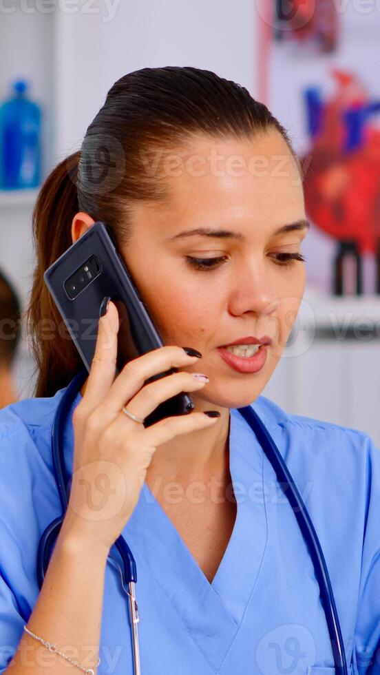 Medical assistant talking at smartphone with doctor asking for advice, typing on laptop, making appointments Healthcare physician in medicine uniform, nurse helping with telehealth communication photo