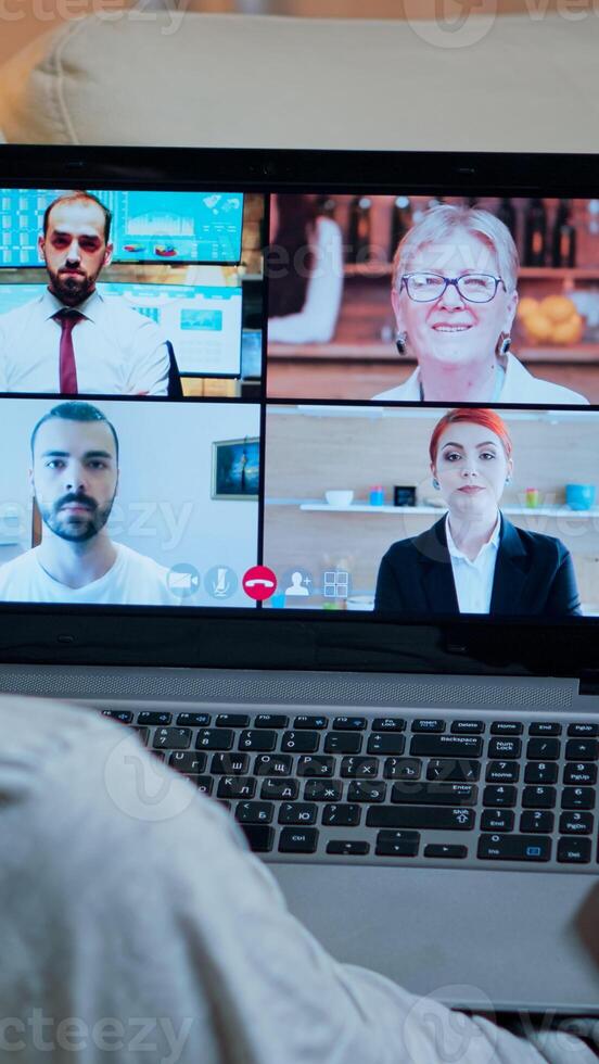 Focused adult using laptop computer during videocall conference talking about social business connection while sitting on couch. Relaxed man working at online communication project overtime in kitchen photo