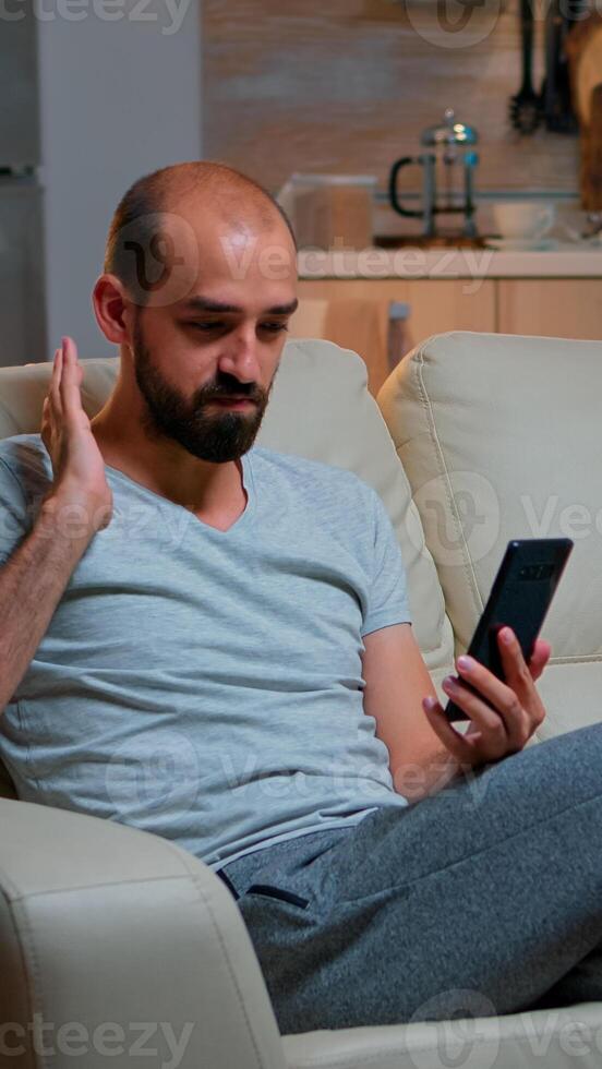 Caucasian male talking with his collegue about business conference using phone while standing in pajamas on couch. Tired man working late at night in kitchen using modern technology wireless photo