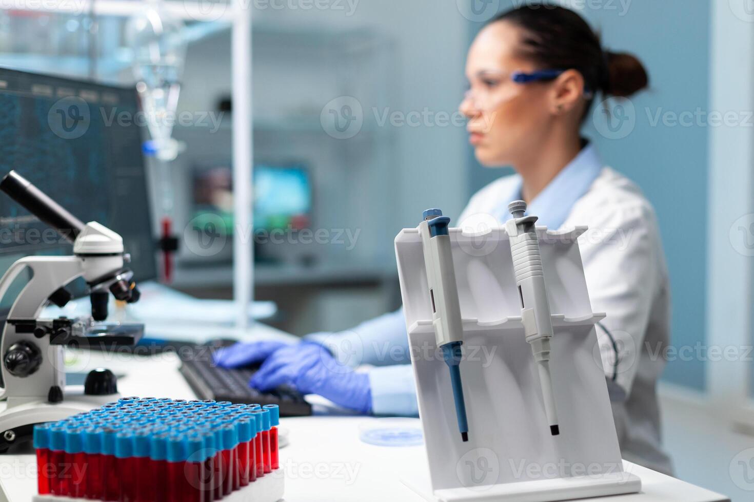 Chemist scientist woman with white coat discovering vaccine against virus typing medical expertise on computer. Professional modern equipment standing on table in hospital laboratory photo