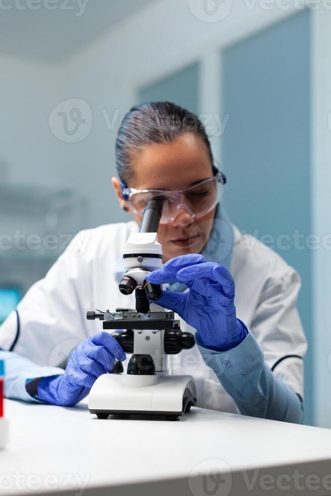 Scientist doctor analyzing blood sample using microscope searching for healthcare treatment developing virus vaccine during medical experiment. Chemist researcher working in hospital laboratory photo