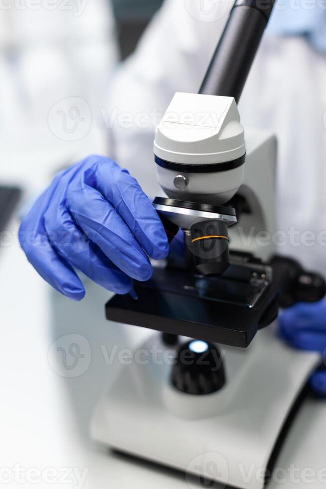 Closeup of biologist woman hands using microscope analyzing blood sample working at virus treatment developing medical vaccine in biochemistry laboratory. Chemistry lab with modern tech photo
