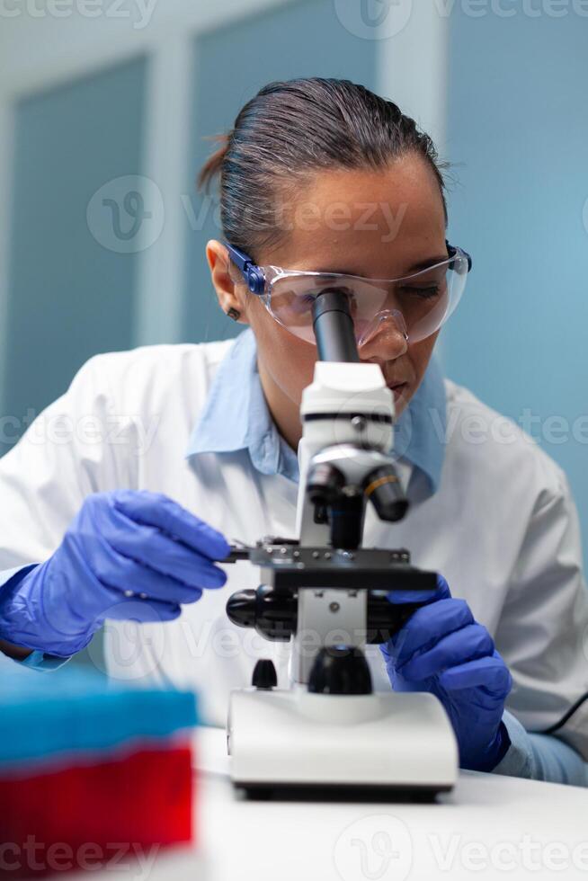 Biologist scientist developing vaccine against virus analyzing blood sample using medical microscope in biochemistry hospital laboratory. Chemist researcher doctor searching for healthcare treatment photo