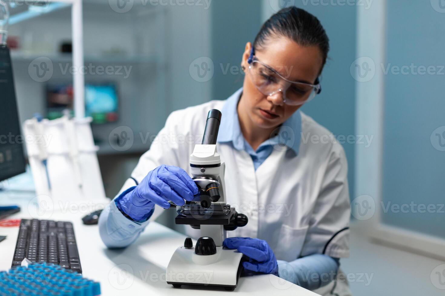 Biologist researcher working at vaccine development against virus putting blood sample under medical microscope during microbiology experiment. Chemist doctor sitting at table in hospital laboratory photo