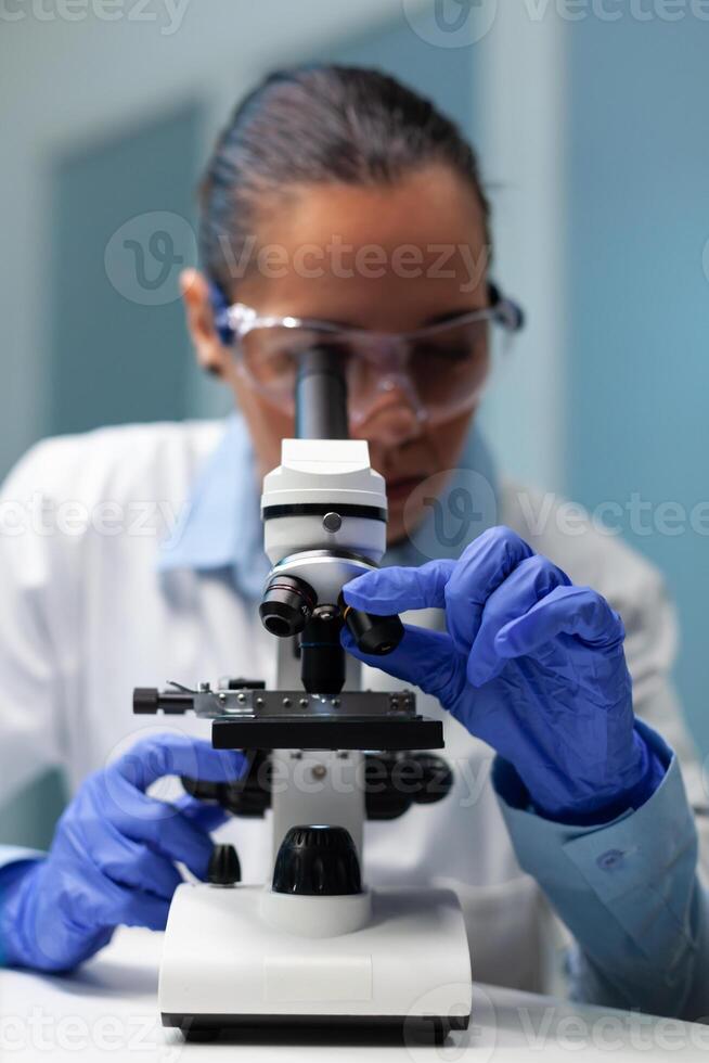 Biologist doctor using medical microscope analyzing blood sample working at microbiology experiment in hospital laboratory. Chemist researcher developing vaccine against virus disease photo