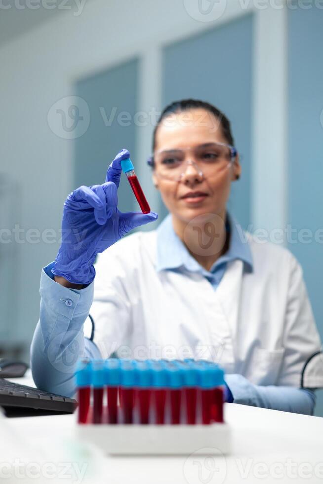 Scientist doctor woman analyzing transparent vacutainer with blood working at microbiology experiment in hospital laboratory. Biologist researcher developing medical vaccine against virus disease photo