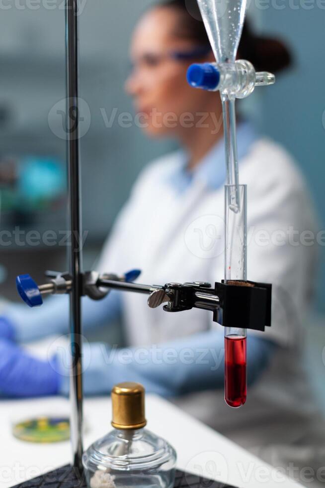 Selective focus on medical industry equipment standing on table, transparent test tube with blood on it. Biologist researcher working in biochemistry hospital laboratory during biochemistry experiment photo